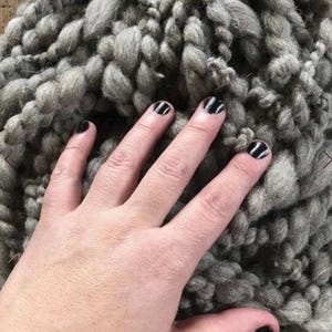 May include: A thick, chunky knit yarn in a neutral gray color. The yarn features a highly textured, irregular surface with varying thicknesses of twisted fibers, creating a dense and voluminous appearance suitable for heavy-duty textile projects.