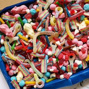 Op de afbeelding: Een blauwe doos vol kleurrijke snoepjes. De mix bevat gummy worms, regenboogriemen, roze muisvormige gummies en diverse andere snoepjes in rood, geel, groen en roze. Een heerlijke traktatie voor elke gelegenheid.