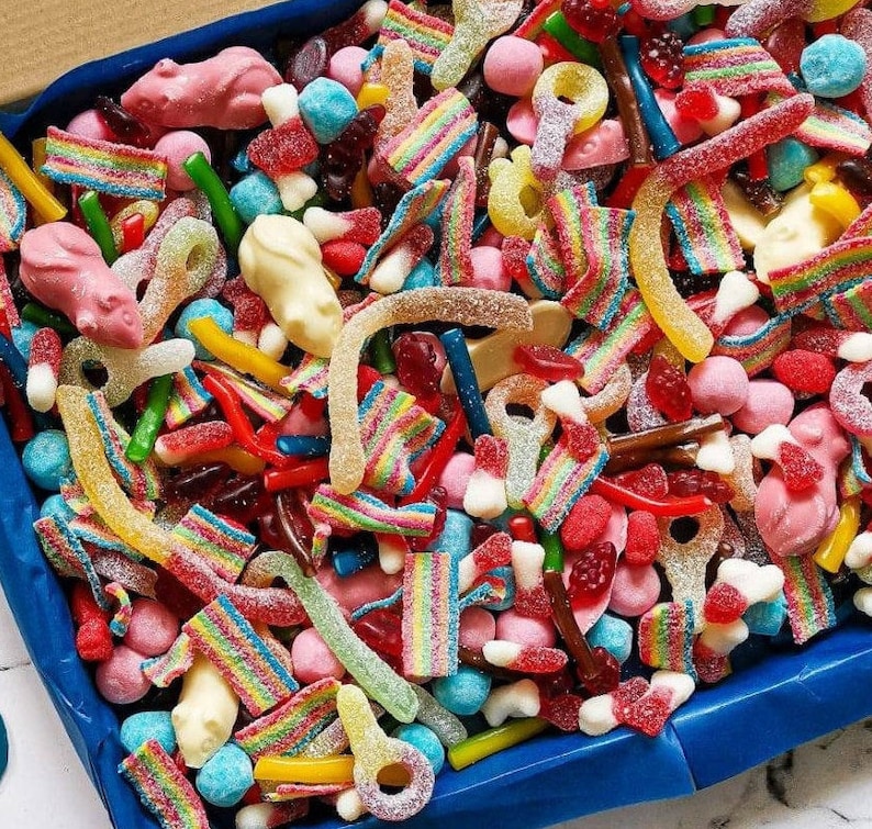 Op de afbeelding: Een blauwe doos vol kleurrijke snoepjes. De mix bevat gummy worms, regenboogriemen, roze muisvormige gummies en diverse andere snoepjes in rood, geel, groen en roze. Een heerlijke traktatie voor elke gelegenheid.