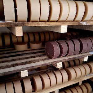 May include: A wooden shelf with multiple rows of round, beige and brown soap bars. The soap bars are stacked neatly on the shelves.