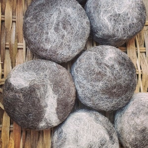 May include: Six brown felted balls with white fibers, arranged in a basket made of woven brown reeds.