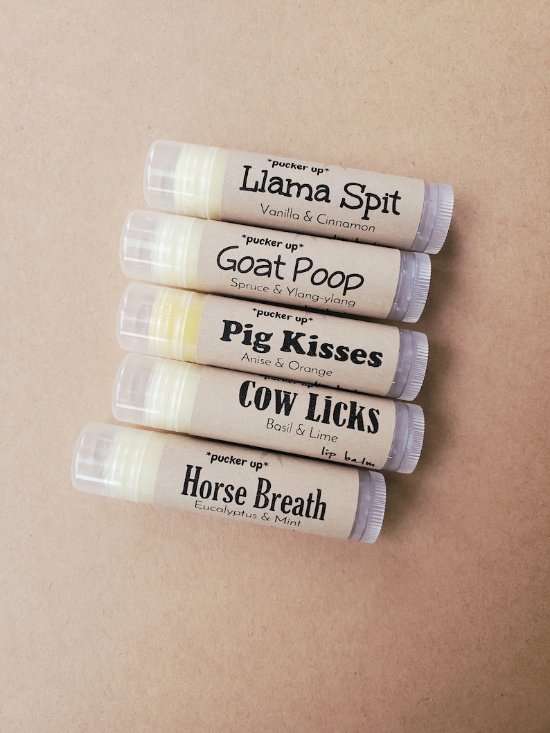 May include: Five lip balm tubes with whimsical names and scents. The tubes are stacked on top of each other. The names are "Llama Spit", "Goat Poop", "Pig Kisses", "Cow Licks", and "Horse Breath".