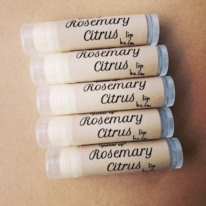 K&ouml;nnte beinhalten: F&uuml;nf braune Lippenbalsam-Tuben mit wei&szlig;en Etiketten. Die Etiketten haben schwarzen Text mit der Aufschrift "Rosemary Citrus lip balm".