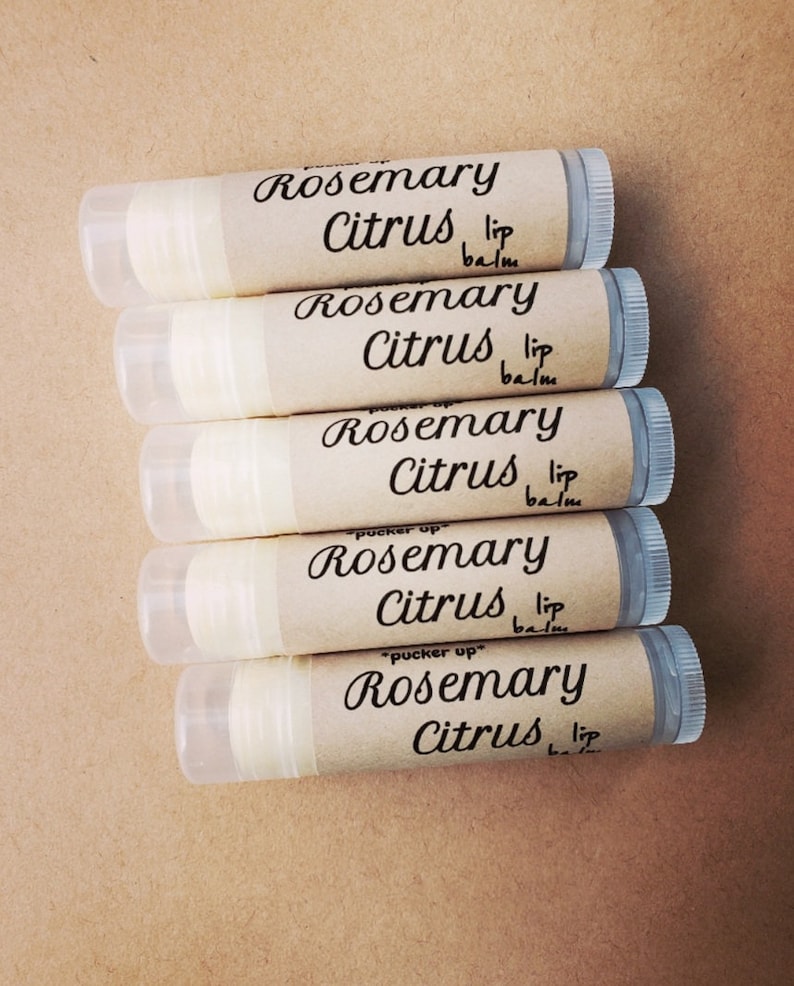 K&ouml;nnte beinhalten: F&uuml;nf braune Lippenbalsam-Tuben mit wei&szlig;en Etiketten. Die Etiketten haben schwarzen Text mit der Aufschrift "Rosemary Citrus lip balm".