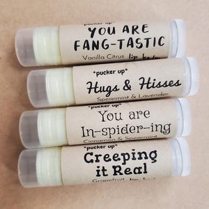 May include: Four lip balm tubes with brown paper labels. The labels have a playful, punny message and list the flavor. The flavors are Vanilla Citrus, Spearmint & Lavender, Cinnamon & Spearmint, and Grapefruit.