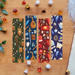 Könnte beinhalten: Vier farbenfrohe Lesezeichen mit Fantasy-Motiven, darunter ein Schild, eine Laute, ein Schwert und Bücher. Die Lesezeichen liegen auf einer Holzoberfläche mit Würfeln und Grünzeug, was eine dekorative Ästhetik erzeugt.