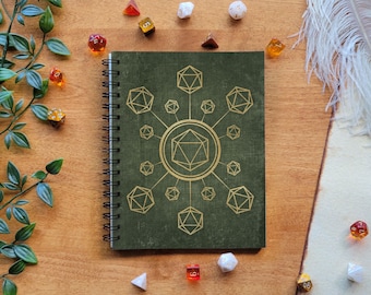 May include: A green spiral bound notebook with a gold design of a 20-sided die in the center surrounded by smaller dice. The notebook is on a wooden surface with dice scattered around it.