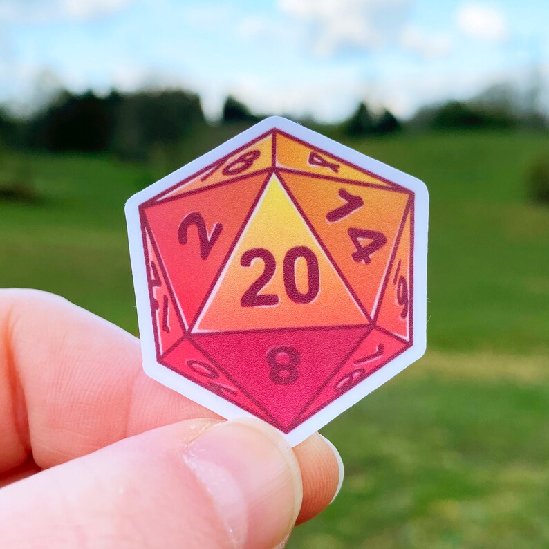 May include: A red, orange and yellow 20-sided die sticker with the numbers 1, 2, 4, 6, 8, 10, 12, 14, 16, 18, 20, 17, 19, 15, 13, 11, 9, 7, 5, and 3.