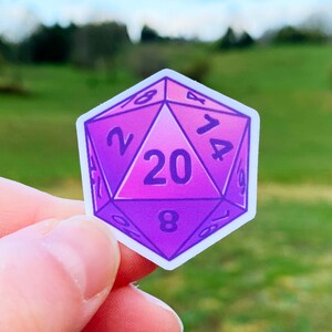 May include: A purple and pink 20-sided die sticker with white numbers. The sticker is shaped like a die and has a gradient colour scheme.