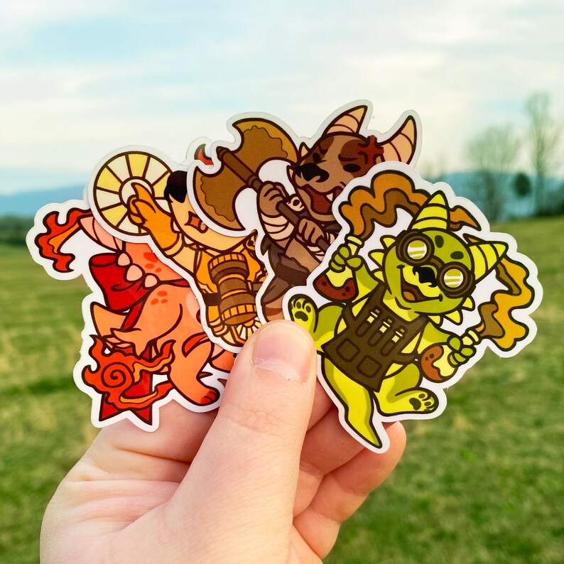 May include: Three colorful cartoon character stickers. The first sticker is a red and orange creature with a large, round head and a long tail. The second sticker is a green and yellow creature with a large, round head and a long tail. The third sticker is a brown and orange creature with a large, round head and a long tail.