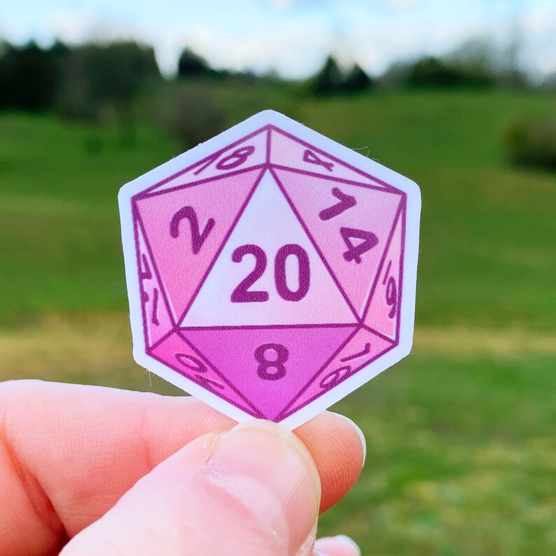 May include: A pink and white 20-sided die with numbers 2, 4, 6, 8, 10, 12, 14, 16, 18, and 20 printed on the faces.