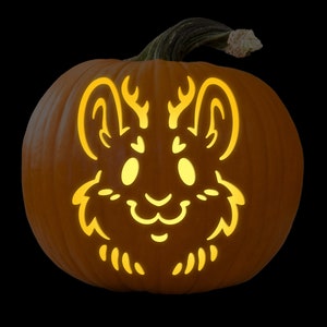 May include: A carved pumpkin with a cute, stylized animal face. The animal has large eyes, a small nose, and antlers. The pumpkin is lit from inside, creating a warm glow.