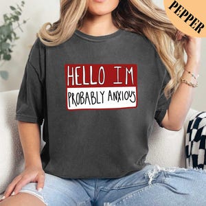 a woman sitting on a couch wearing a black shirt with the words hello i '
