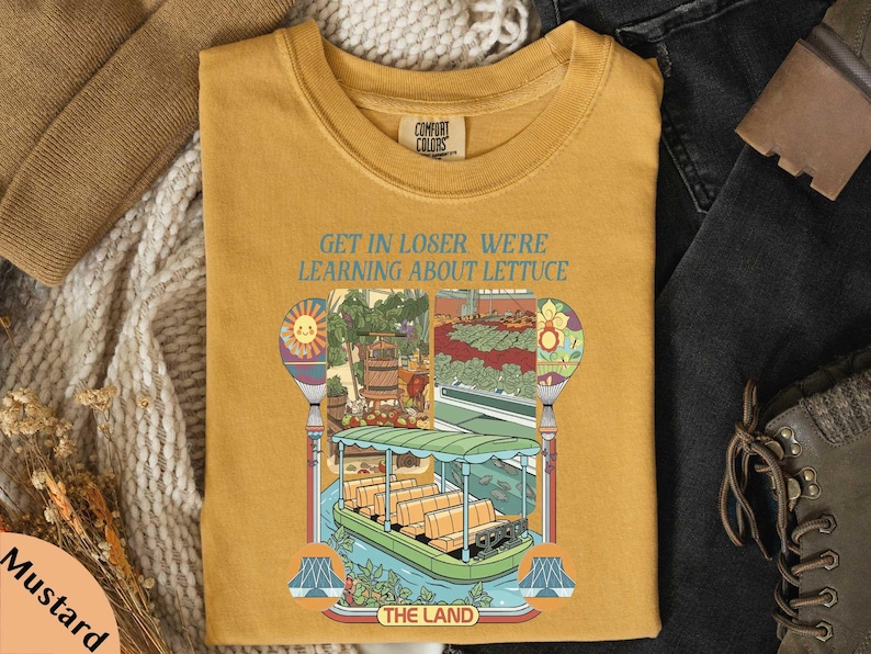 a yellow t-shirt with a colorful illustration of a boat and a sign that says "GET IN LOSER WE'RE LEARNING ABOUT LITTUCE" printed on it.
