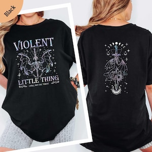 May include: Black t-shirt with a front graphic that reads "VIOLENT LITTLE THING I WILL NOT DIE TODAY" with a sword, wings, and stars design. The back of the shirt features a similar design with a sword, dragon, and moon phases.