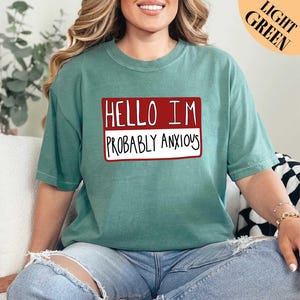 a woman sitting on a couch wearing a t - shirt that says hello i '