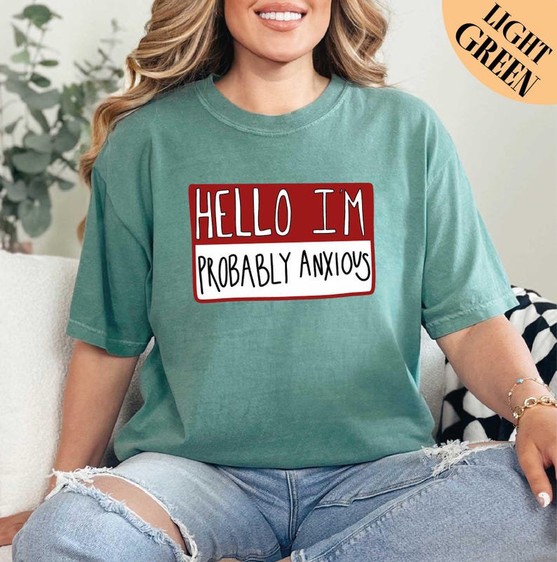 a woman sitting on a couch wearing a t - shirt that says hello i '