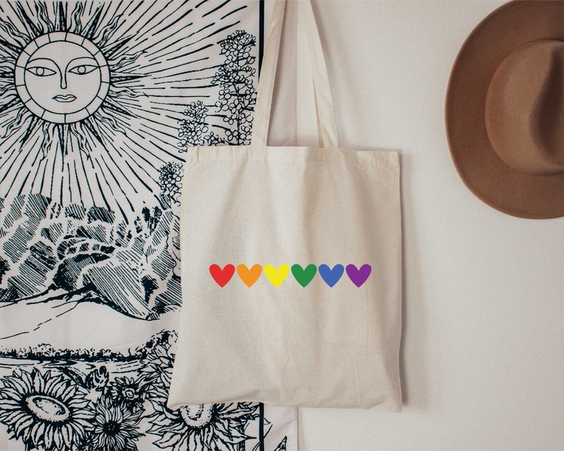May include: A white tote bag with a rainbow of hearts printed on the front. The hearts are red, orange, yellow, green, blue, and purple.