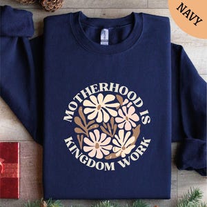 May include: Navy blue sweatshirt with a white circle design featuring a floral pattern and the text "Motherhood is Kingdom Work".