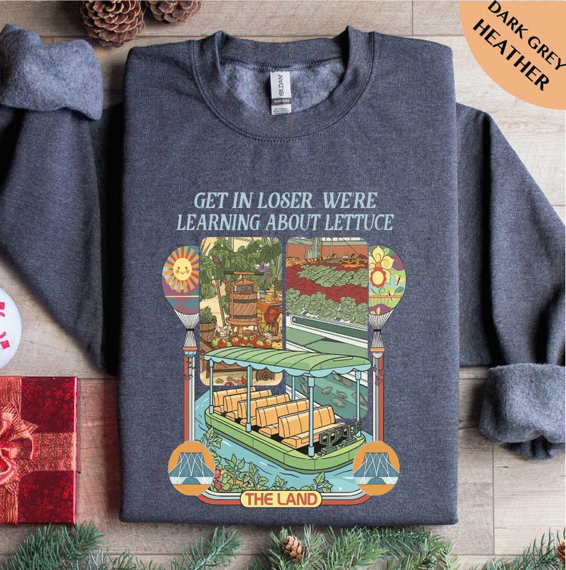 A gray sweatshirt with a colorful graphic design depicting a boat and a garden scene, along with text that reads "GET IN LOSER WE'RE LEARNING ABOUT LECTUCE THE LAND".