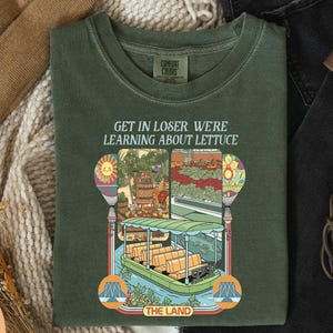 a green t-shirt with a colorful illustration of a boat and a sign that says "GET IN LOSER WE'RE LEARNING ABOUT Lettuce".