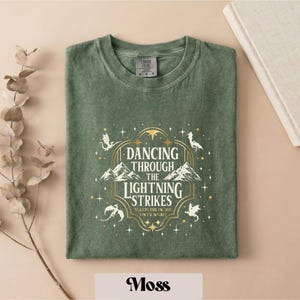 A green t-shirt with a graphic design featuring a dragon and stars, along with the text "DANCING THROUGH THE LIGHTNING STRIKES ON NIGHT".