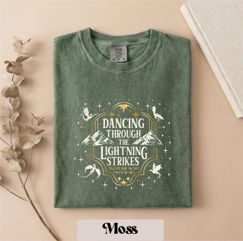 A green t-shirt with a graphic design featuring a dragon and stars, along with the text "DANCING THROUGH THE LIGHTNING STRIKES ON NIGHT".