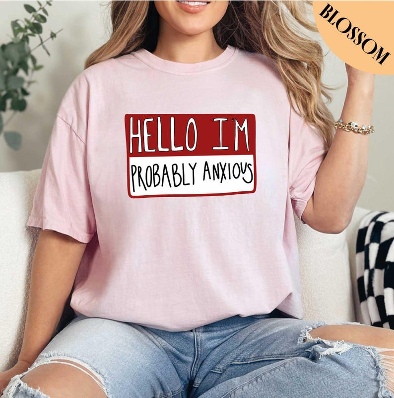 May include: A pink t-shirt with a red name tag that says "Hello I'm Probably Anxious".