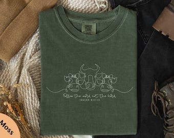 May include: Moss green t-shirt with a white line drawing of three cows and the text "Follow the word, not the herd" from Isaiah 8:11-13. The shirt is made of a soft, comfortable material.