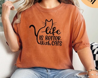 Può includere: Una maglietta color arancio bruciato con una silhouette di gatto nero e il testo "life is better with cats".