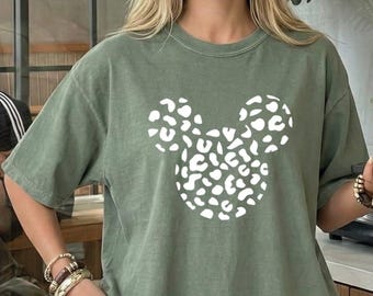 May include: A moss green short-sleeved t-shirt featuring a white graphic of a mouse head silhouette filled with a leopard print pattern. The shirt has a crew neckline and a relaxed fit, with the word moss printed in a small box at the top left.