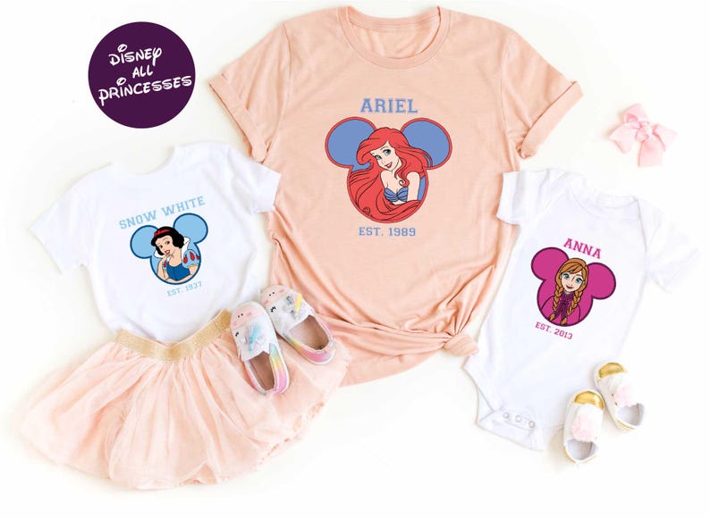 Disney Princess-themed clothing and accessories, including a pink t-shirt with the character Ariel, a white t-shirt with the character Snow White, and a pink onesie with the character Anna.