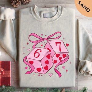 A t-shirt with a graphic design featuring two pink dice with the number 6 on them, surrounded by hearts and ribbons.