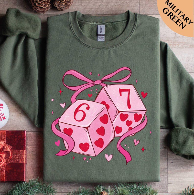A green t-shirt with a graphic design featuring two pink dice with the number 6 and 7 on them, surrounded by hearts and ribbons.