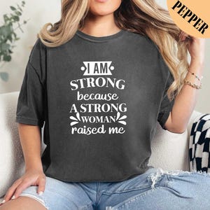 a woman wearing a black shirt that says i am strong because a strong woman raised