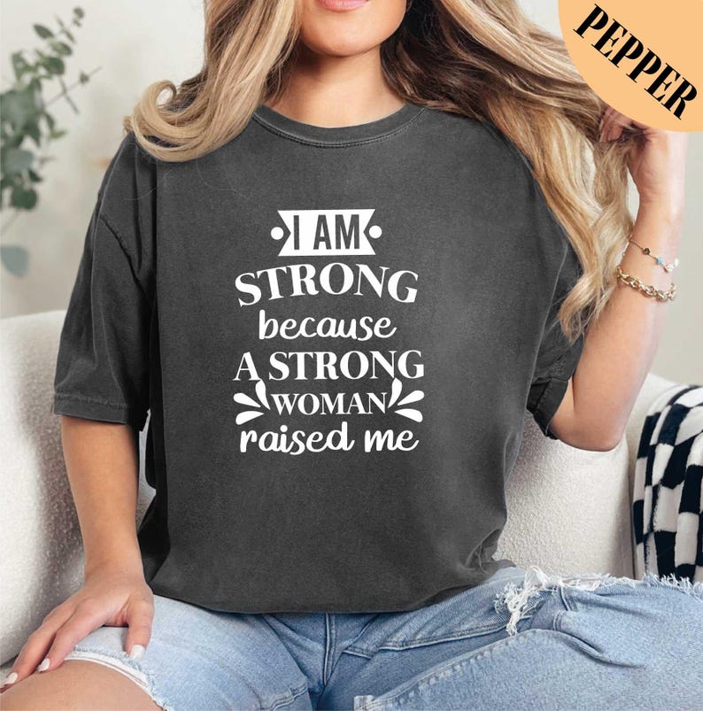a woman wearing a black shirt that says i am strong because a strong woman raised