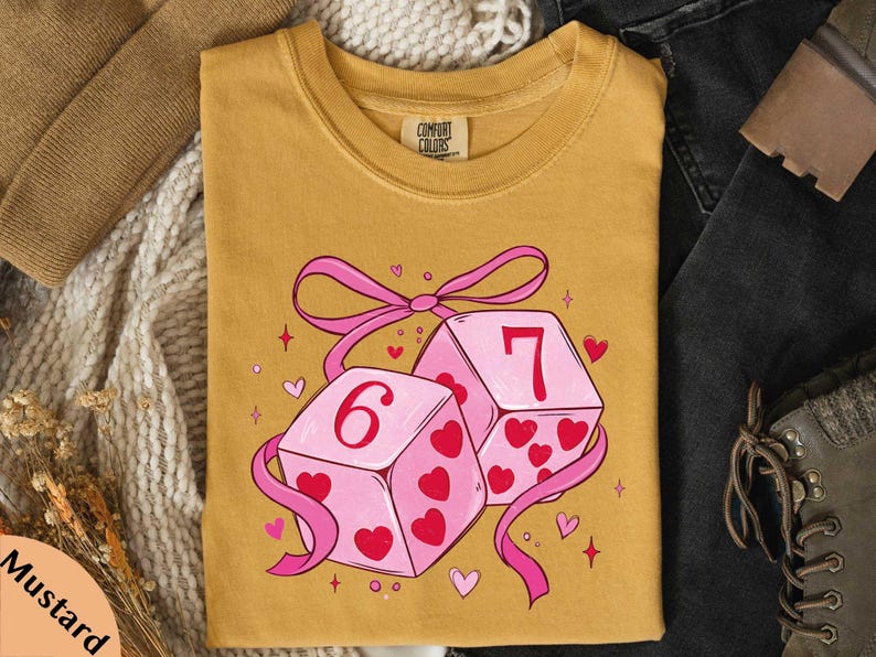 a yellow t-shirt with a graphic design of two pink dice with the number 6 on them, surrounded by hearts and ribbons.