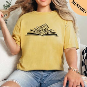 May include: A mustard yellow t-shirt with a black outline of an open book with flowers growing from the pages.