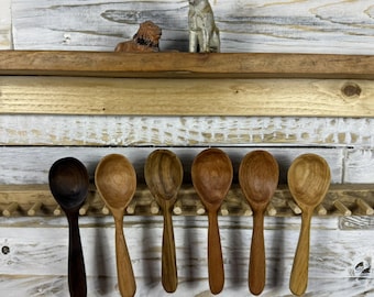 Könnte beinhalten: Sechs Holzlöffel in verschiedenen Brauntönen werden auf einem Holzregal präsentiert. Zwei kleine Löwenfiguren sitzen auf einem Regal darüber. Die Löffel sind aus verschiedenen Holzarten gefertigt.