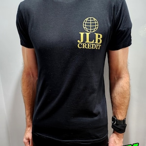 Könnte beinhalten: Schwarzes T-Shirt mit Rundhalsausschnitt und goldenem Logo "JLB CREDIT" mit einem Globus-Motiv. Das Shirt besteht aus einem weichen Material. Der Text "VANITY PUBLISHING" befindet sich unten.