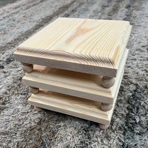 May include: Three stacked wooden square coasters with rounded edges and small wooden knobs on the bottom of each coaster.