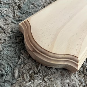 May include: A light wood plaque with a decorative, scalloped edge. The plaque is unfinished and ready to be painted or stained.