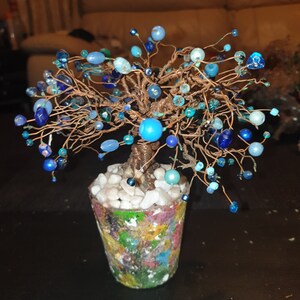 May include: A wire tree sculpture with blue and turquoise beads, in a colourful painted pot with white stones.