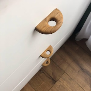 May include: Three wooden drawer pulls with a rounded, half-circle shape and a circular cutout in the center. The pulls are arranged vertically, with the largest pull at the top and the smallest pull at the bottom.