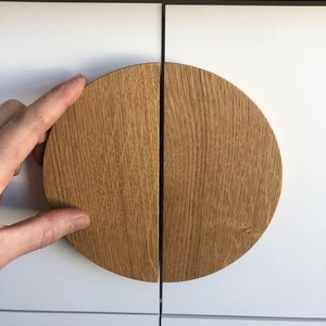 May include: Close-up of a pair of white cabinet doors with a circular wooden handle. The handle is made of light brown wood and is split in half, with each half on a separate door. The top of the cabinet is a dark brown wood.