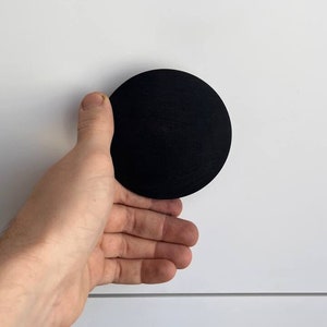 May include: A black round cabinet knob with a smooth surface. The knob is mounted on a white cabinet door.