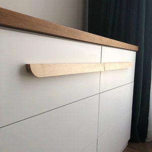 Puede incluir: Cómoda blanca con seis cajones y una encimera de madera. Los cajones tienen tiradores de madera.