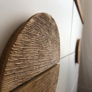 May include: Close-up of a wooden cabinet door with a unique, textured, half-circle handle. The handle is made of light brown wood with a rough, carved surface.