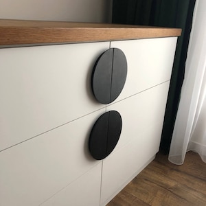 May include: White dresser with four drawers and black round drawer pulls. The dresser has a wood top.