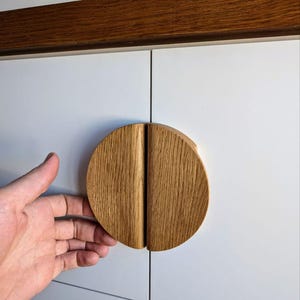 May include: A round wooden cabinet knob with a split design. The knob is made of light brown wood and is mounted on a white cabinet door.